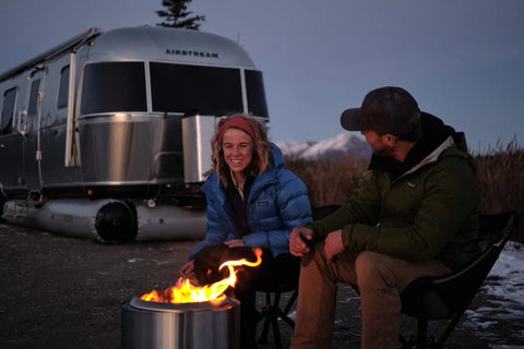 AIRSKIRTS Inflatable RV Skirt - Couple at Campfire Beside Skirted Airstream at Winter Dusk | United RV Parts